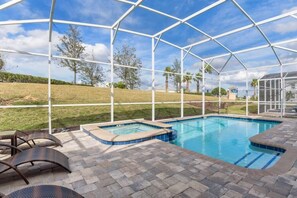 A covered outdoor swimming pool with a hot tub, surrounded by a white metal frame and a brick patio.