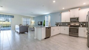 A modern kitchen with white cabinetry, stainless steel appliances, and a grey tiled floor. - C9052sid- The Retreat at Champions Gate (Davenport)