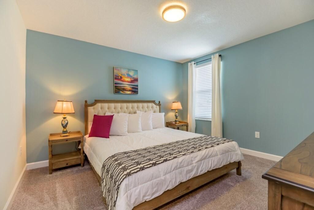 A bedroom with a large bed, two bedside tables with lamps, a headboard, and a painting on the wall.