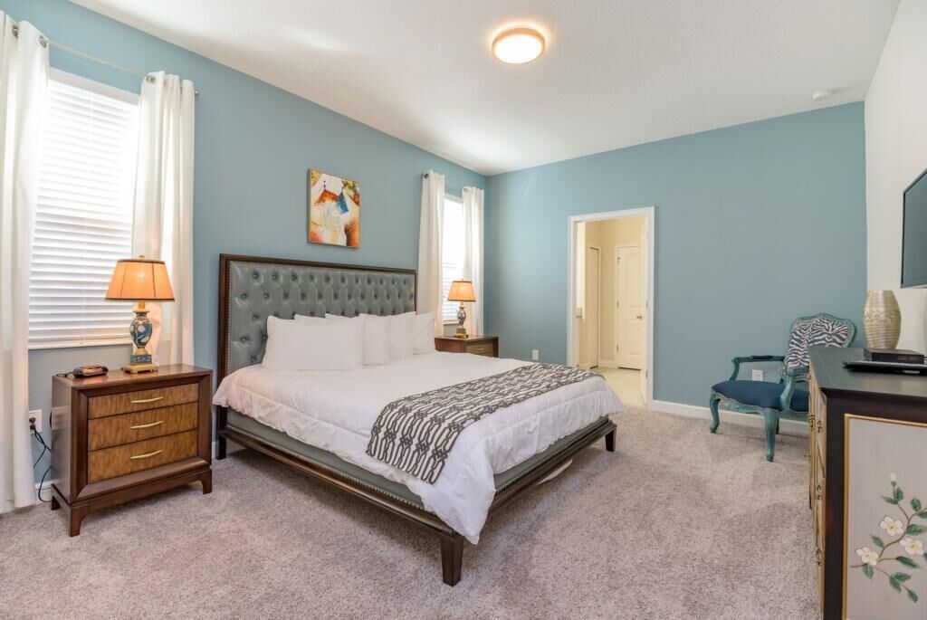 A bedroom with a large bed, two bedside tables, a chair, and a door.