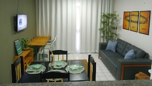 A living room with a dining area, a television mounted on the wall, and three framed pictures on the wall. - Just a few steps from the beach - Ground-floor 2-bedroom apartment, swimming pools, AC, Wi-Fi, garage (Fortaleza)