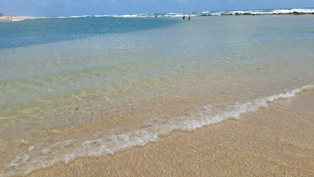 A beach with clear shallow waters, a sandy shore, and a distant rocky coastline. - Just a few steps from the beach - Ground-floor 2-bedroom apartment, swimming pools, AC, Wi-Fi, garage (Fortaleza)