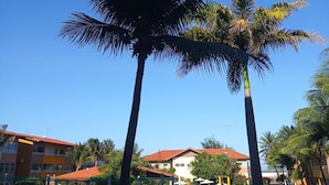 A clear blue sky with a large palm tree in the foreground and a building with a red roof in the background. - Just a few steps from the beach - Ground-floor 2-bedroom apartment, swimming pools, AC, Wi-Fi, garage (Fortaleza)