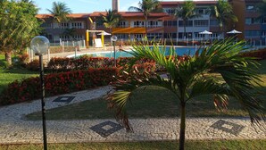 A hotel with a swimming pool, palm trees, and a tiled walkway. - Just a few steps from the beach - Ground-floor 2-bedroom apartment, swimming pools, AC, Wi-Fi, garage (Fortaleza)