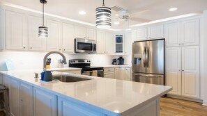 Une cuisine moderne avec des armoires blanches, des appareils en acier inoxydable, un grand îlot central et des luminaires suspendus.