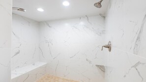 A bathroom with white marble tiles, a showerhead, a sink, and a shelf.