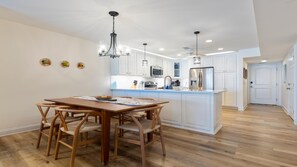 A modern kitchen with white cabinetry, a central island, and a dining area with wooden furniture.