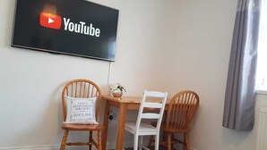 A room with a flat-screen TV displaying the YouTube logo, a wooden table, and two wooden chairs. - Caspian House (4 Bedrooms) - Serviced Accommodation (Grimsby)