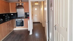 A kitchen with wooden cabinets, a stove, and a modern pendant light. - Caspian House (4 Bedrooms) - Serviced Accommodation (Grimsby)