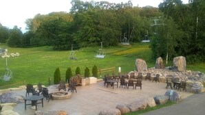 Un espace extérieur aménagé avec des chaises Adirondack et des tables, un foyer et une vue sur un télésiège en arrière-plan.