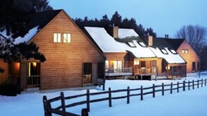 Une rangée de cabanes en bois, avec un sol enneigé et une clôture en bois au premier plan.