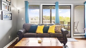 Ein Wohnzimmer mit einem dunkelbraunen Ledersofa, einem Holztisch und Blick durch große Schiebeglasfenster ins Freie.