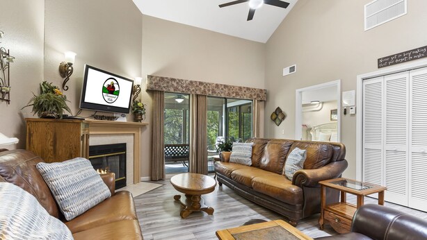 A living room with a fireplace, leather sofas, a coffee table, and a television displaying a logo. - 4BR, 3BA Golf Condo Ticket Deals and Resort Amenities (Branson)