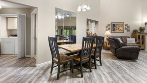 Een eetruimte met een houten tafel en stoelen, een grote spiegel en een plafondlamp.