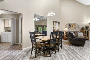 A dining area with a wooden table and chairs, a large mirror, and a ceiling light fixture.