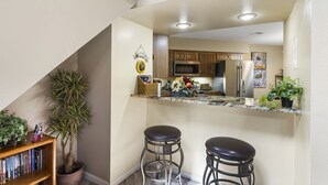 A kitchen with a granite countertop, wooden cabinets, a stainless steel refrigerator, and a microwave. There are two bar stools and a potted plant. - 4BR, 3BA Golf Condo Ticket Deals and Resort Amenities (Branson)