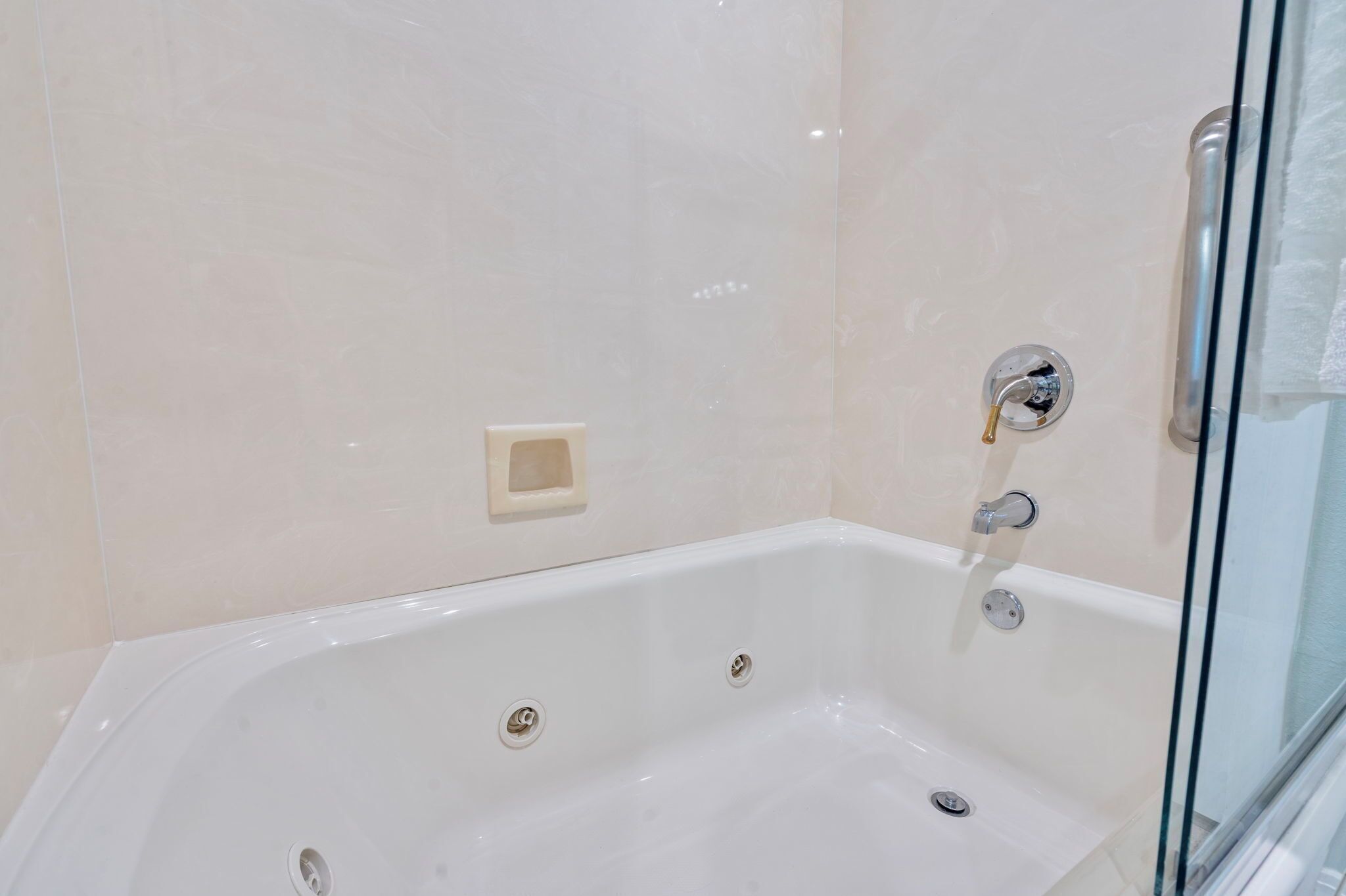 A modern bathroom with a white bathtub, a glass shower enclosure, and a small beige soap dish on the wall.