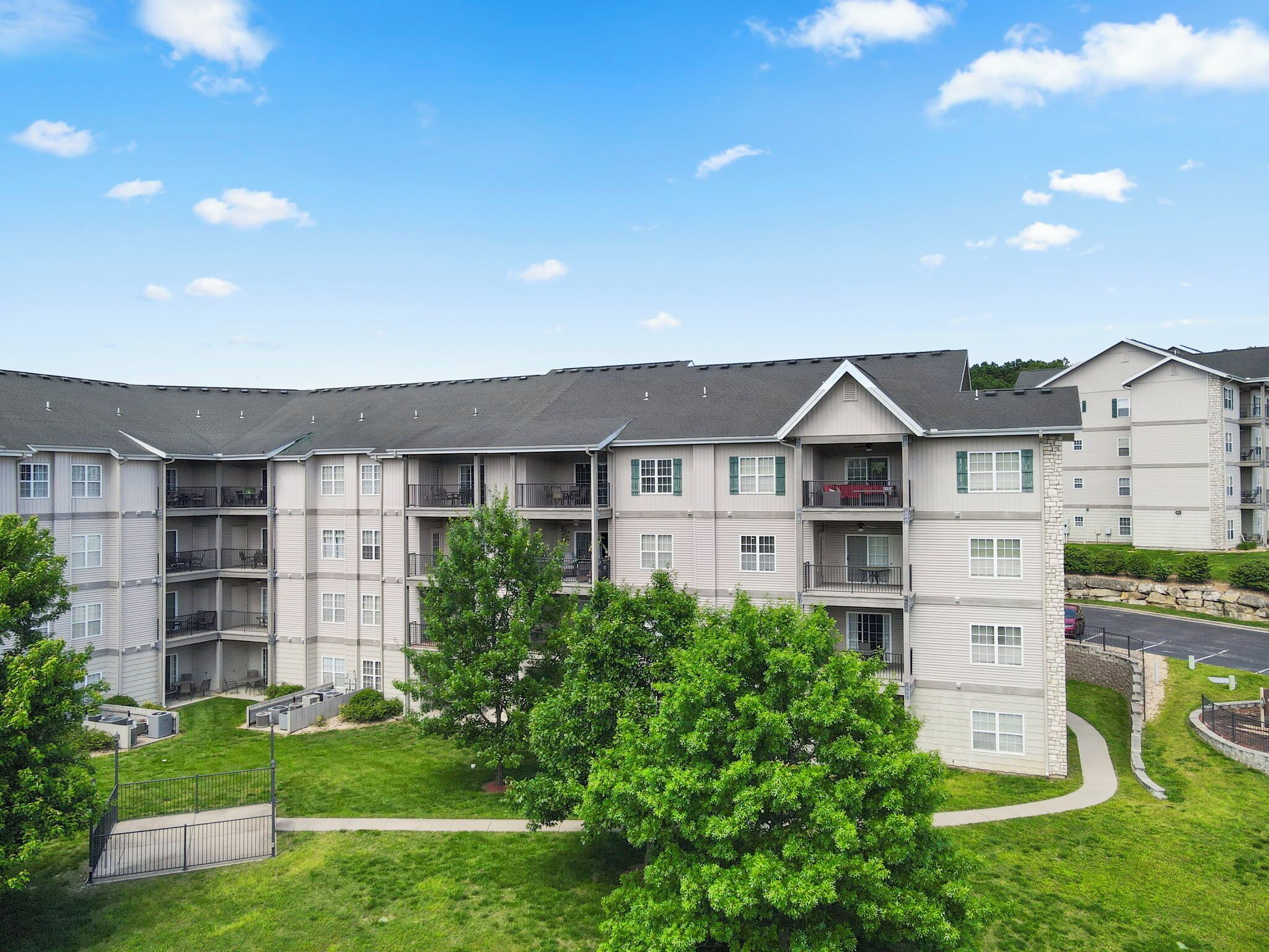 A multi-story residential building with balconies, a lawn, and a stone wall.