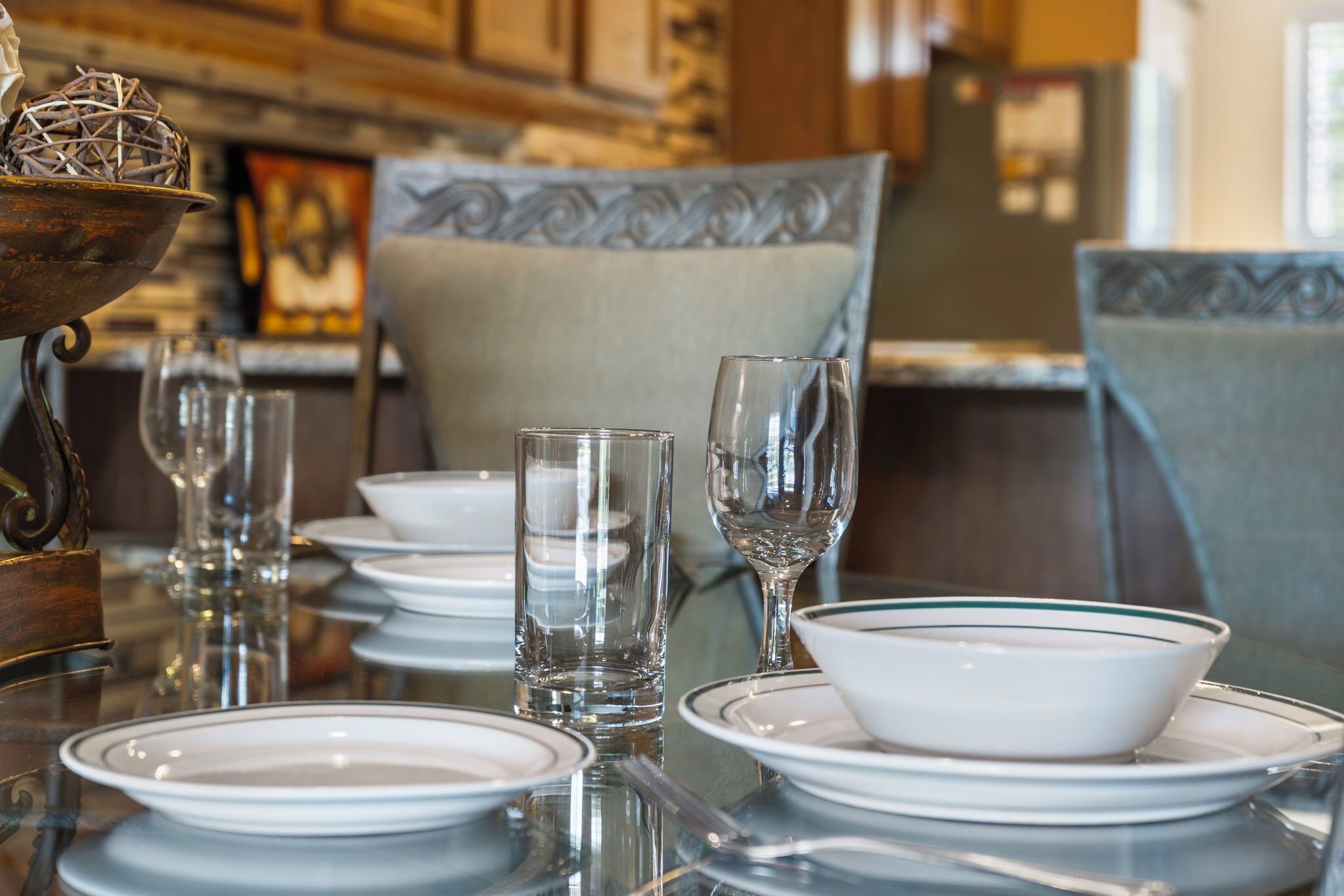 A dining table set with white plates, bowls, and clear glasses, with a decorative metal bowl on the left.