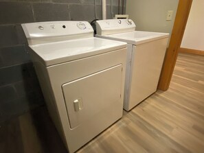 A laundry room with two white front-loading washers and dryers, a tiled wall, and a wooden floor. - Next to Rocky Top Sports! 5 King bedrooms 4 Bath Family-Friendly Sleeps 18 (Gatlinburg)