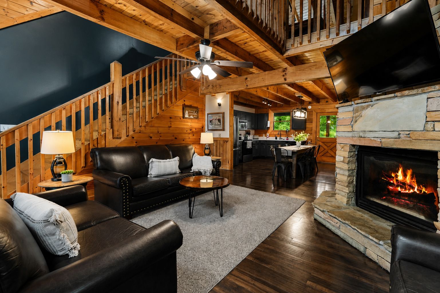 A cozy living room with a fireplace, a staircase, and a kitchen area.