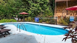 A swimming pool with a wooden deck, surrounded by lush greenery and a stone wall. - Next to Rocky Top Sports! 5 King bedrooms 4 Bath Family-Friendly Sleeps 18 (Gatlinburg)