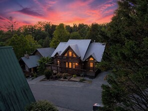 A log cabin with a balcony, surrounded by trees, during twilight. - Next to Rocky Top Sports! 5 King bedrooms 4 Bath Family-Friendly Sleeps 18 (Gatlinburg)