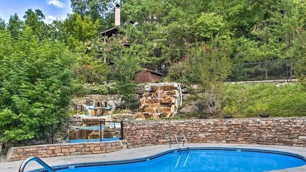 A swimming pool with a stone wall and a wooden deck. - Next to Rocky Top Sports! 5 King bedrooms 4 Bath Family-Friendly Sleeps 18 (Gatlinburg)