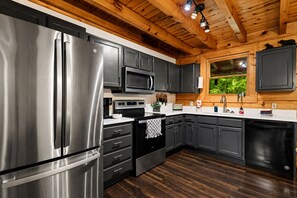 A modern kitchen with stainless steel appliances, dark cabinetry, and a wooden ceiling.