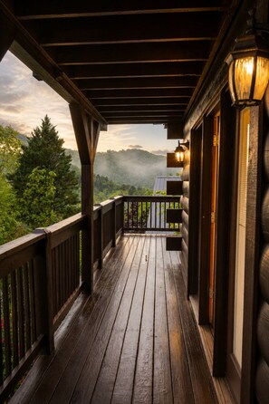 A wooden deck with a railing, a lantern, and a view of a forested landscape. - Next to Rocky Top Sports! 5 King bedrooms 4 Bath Family-Friendly Sleeps 18 (Gatlinburg)