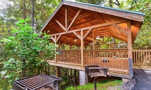 A wooden deck with a metal grill, surrounded by trees.