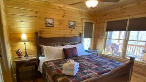 Un dormitorio de cabaña de madera con una cama, una mesita de noche, una lámpara y un ventilador de techo.