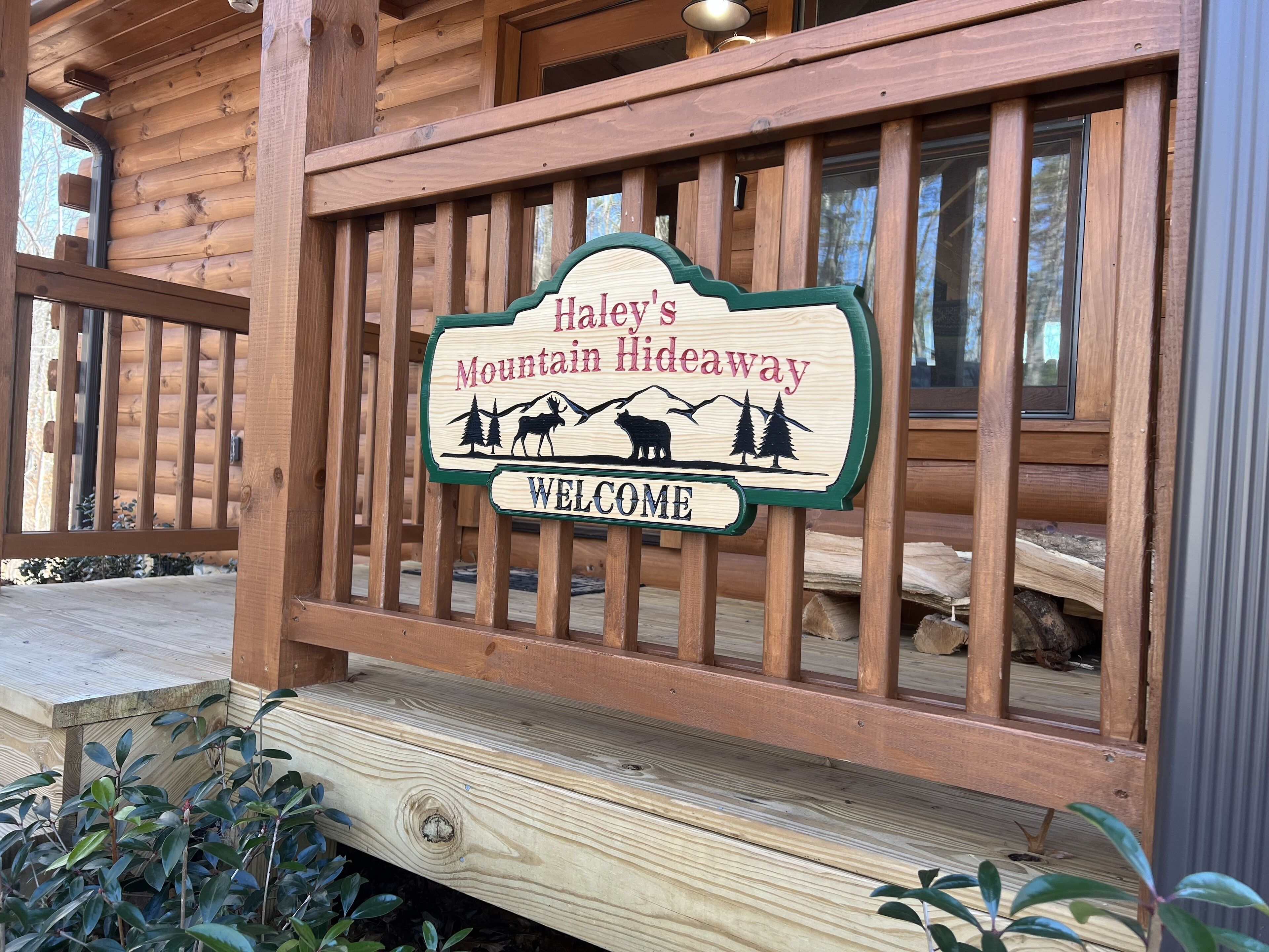 A wooden sign with the text "Haley's Mountain Hideaway" and "WELCOME" on a porch railing.