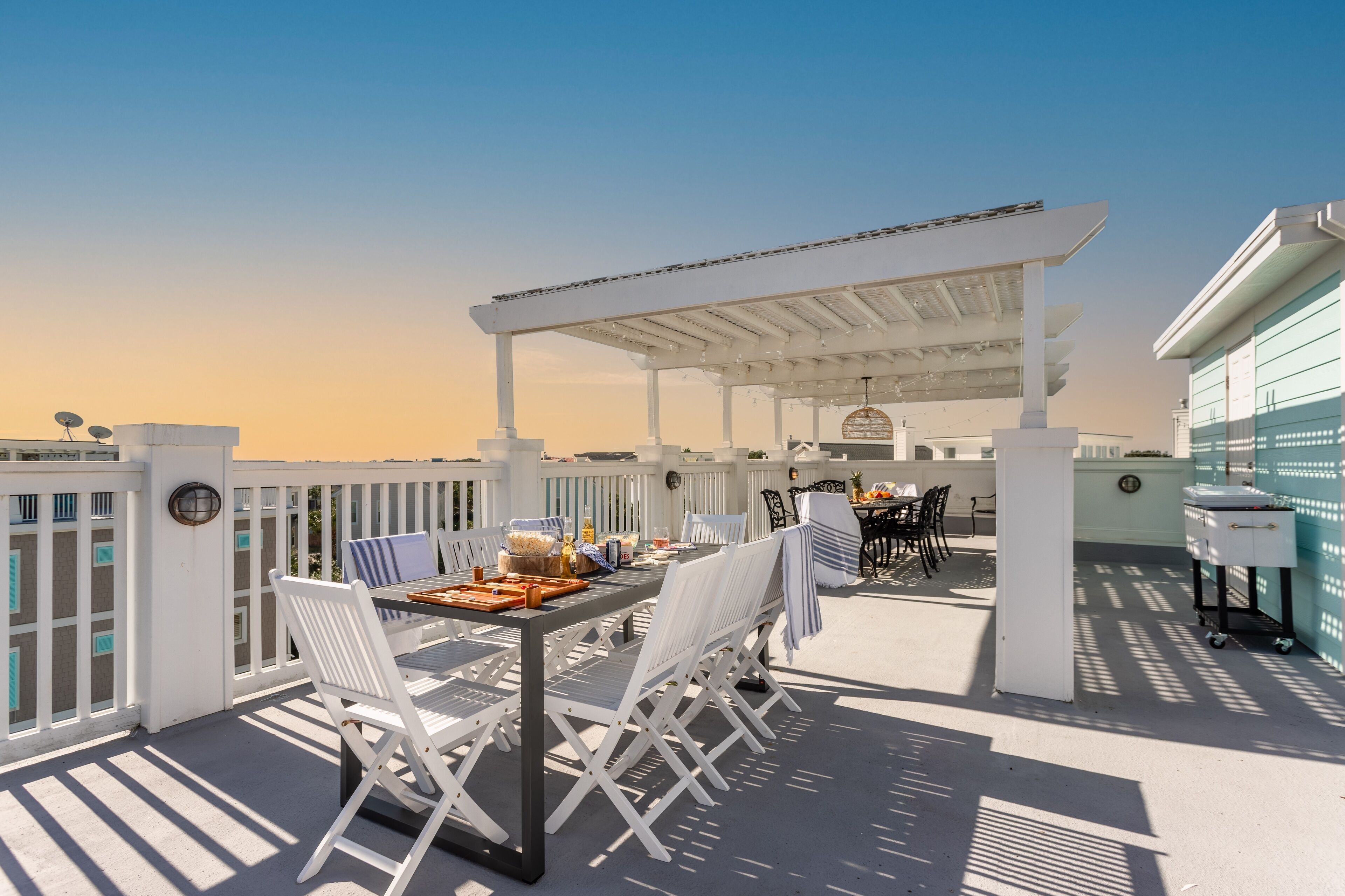An outdoor patio with a pergola, white chairs, and a dining table set for two.