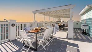 Eine Terrasse im Freien mit einer Pergola, weißen Stühlen und einem Esstisch für zwei Personen.