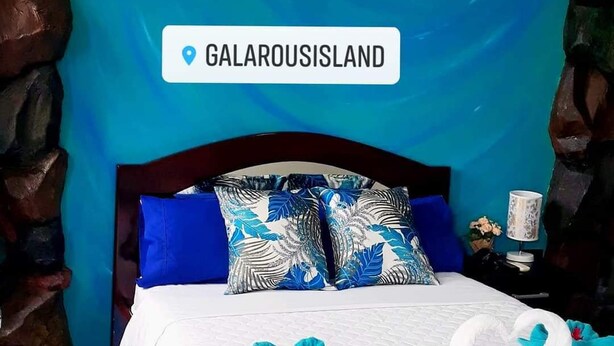 Una camera d'albergo con arredamento a tema blu, che include un quadro di un delfino sulla parete, un letto con copripiumino bianco e blu e cuscini con motivi a foglia tropicale.