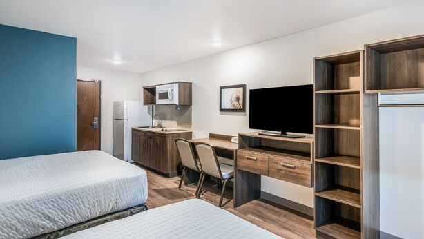 A modern hotel room with two beds, a kitchenette, a desk with a chair, a television, and built-in shelving. - Extended Stay America Select Suites Orlando Kissimmee (Kissimmee)