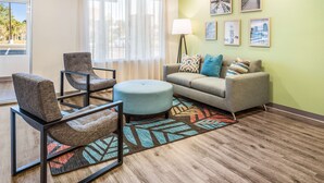 A modern living room with a sofa, armchair, ottoman, and a floor lamp. - Extended Stay America Select Suites Orlando Kissimmee (Kissimmee)