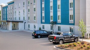 A multi-story hotel with a blue and white exterior, parking lot, and two parked vehicles. - Extended Stay America Select Suites Orlando Kissimmee (Kissimmee)