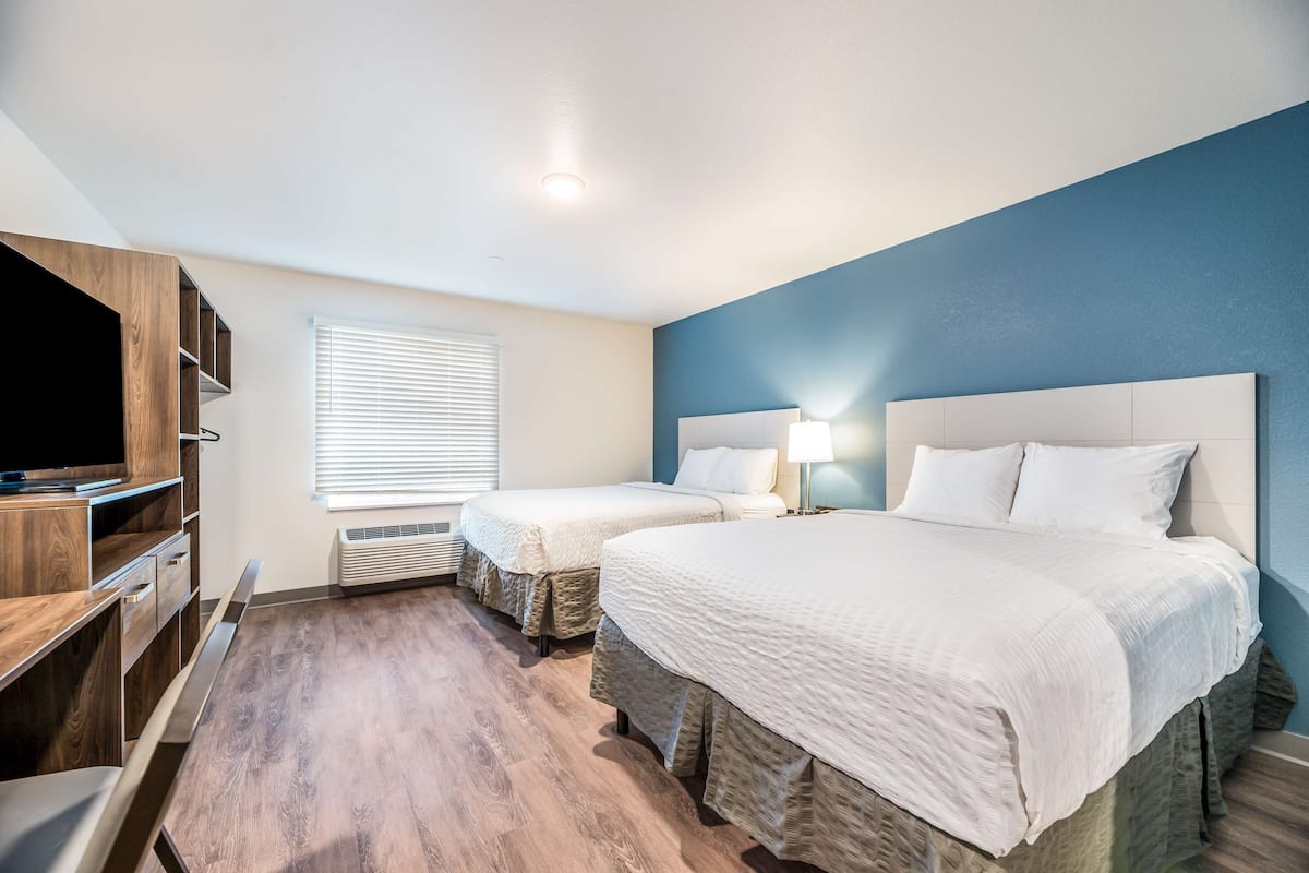 Quarto de hotel com duas camas, uma televisão e uma escrivaninha.