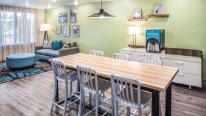 A modern hotel room with a wooden dining table, white chairs, a sofa, and a coffee machine. - Extended Stay America Select Suites Orlando Kissimmee (Kissimmee)