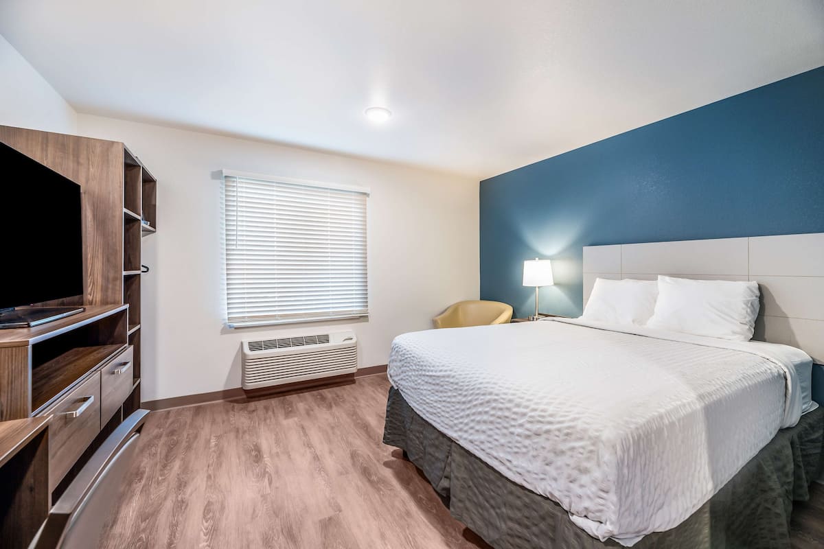 Quarto de hotel com cama, televisão, cadeira e abajur.