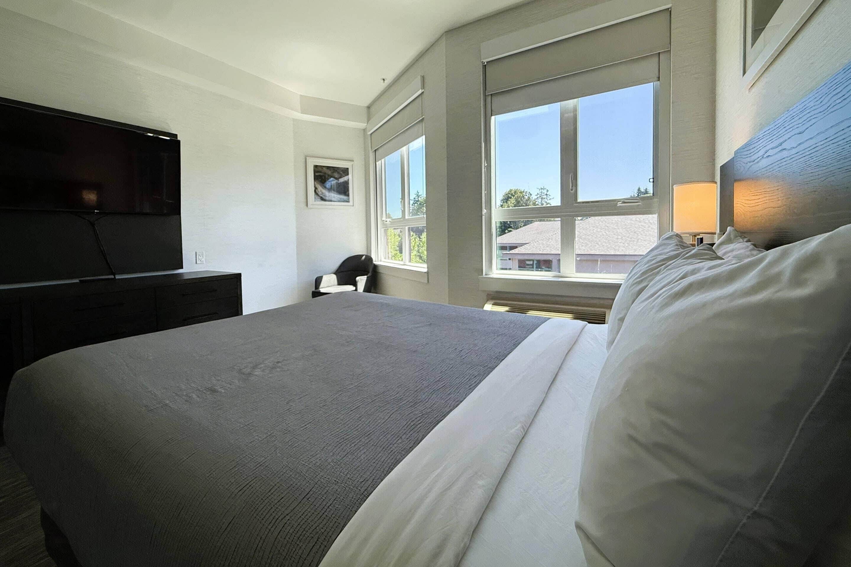 A hotel room with a bed, a flat-screen TV, a desk, and a window with a view of buildings.