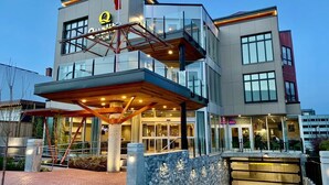 Un hotel moderno con fachada de vidrio, una entrada destacada con toldo de madera y un letrero de restaurante visible.