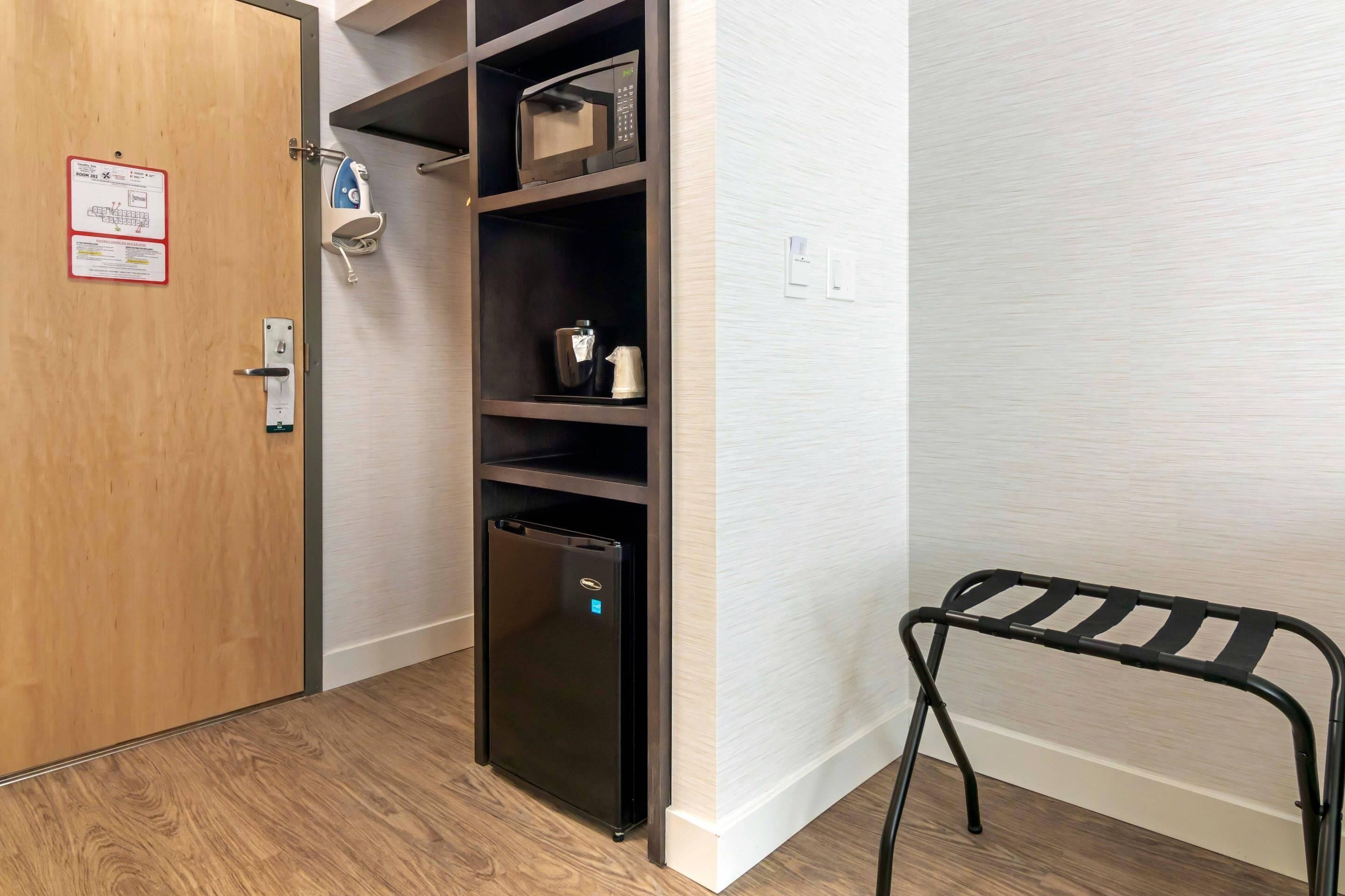 A compact room with a built-in refrigerator, a microwave, and a small shelf with a kettle and a cup.