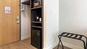 A compact room with a built-in refrigerator, a microwave, and a small shelf with a kettle and a cup.