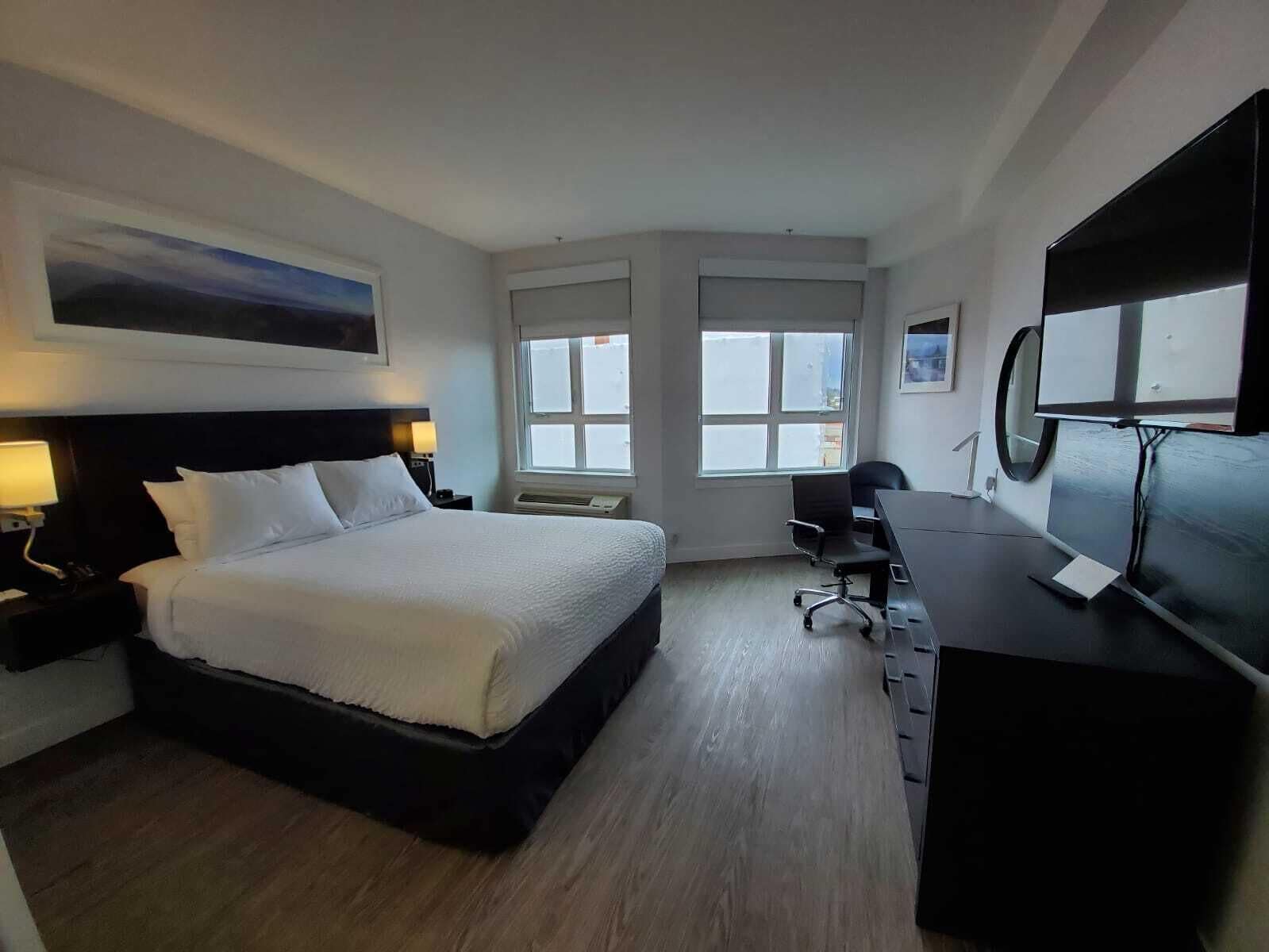 A hotel room with a bed, desk, chair, and a TV.