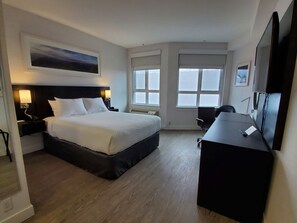 A hotel room with a bed, bedside tables, a desk, a chair, and a TV. - Quality Inn (Nanaimo)