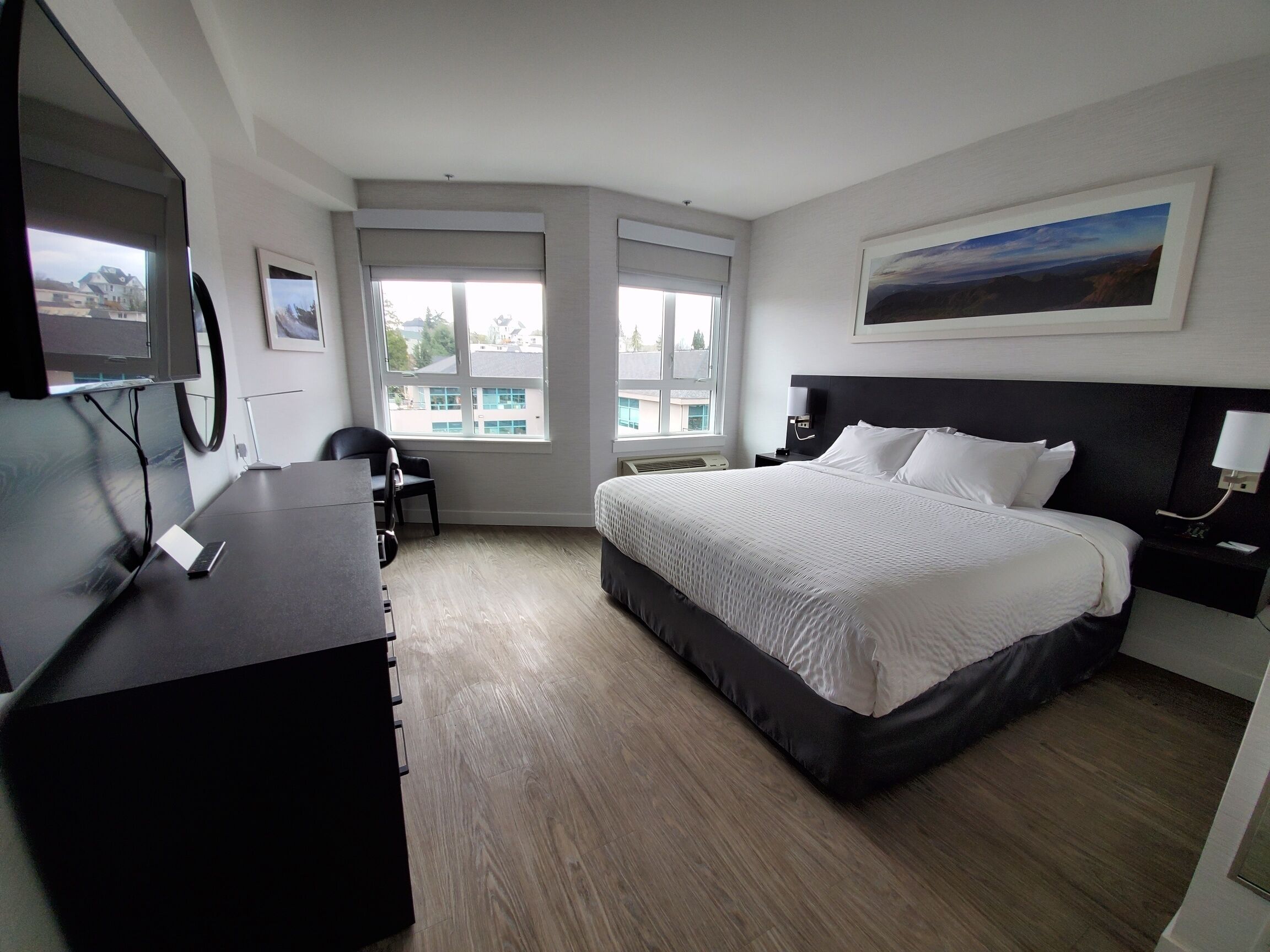 A hotel room with a bed, a desk, a chair, a TV, and large windows.