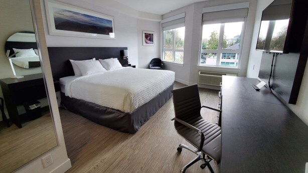 Una habitación de hotel moderna con una cama grande, un escritorio con una silla, un televisor y una ventana con vistas al exterior.